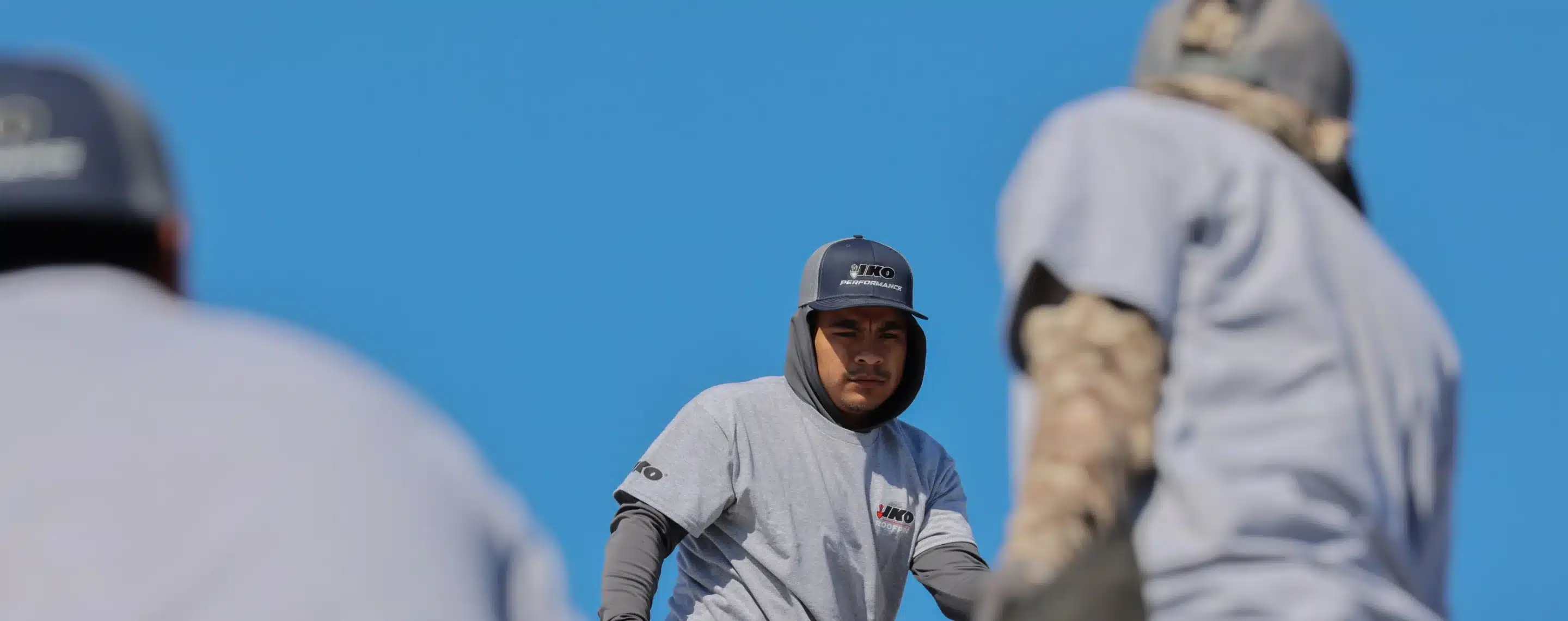 Construction worker in front of a bright blue sky wearing and IKO hat and tshirt.